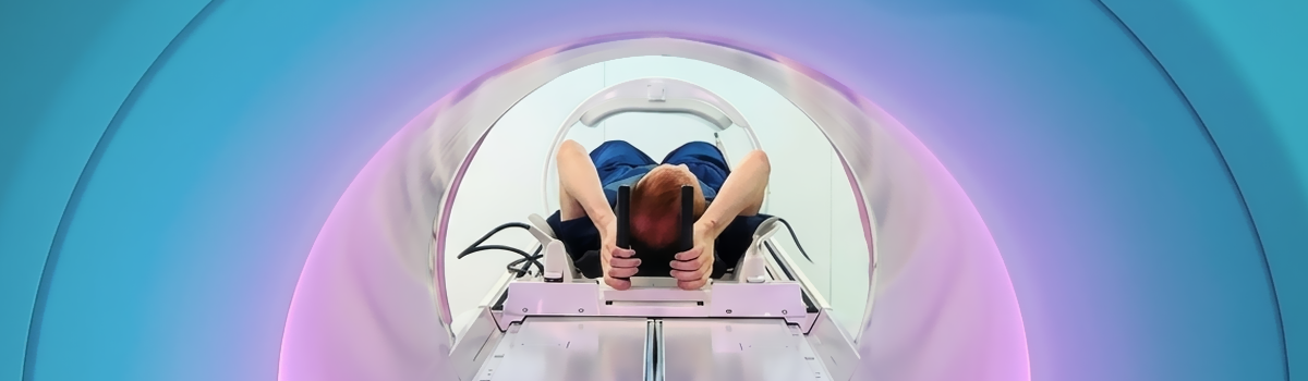 A person is lying down in the opening of a large round MRI imaging device. It is lit with pastel blue and purple hues. the person's face cannot be seen, the view is from behind them, through the big round opening.